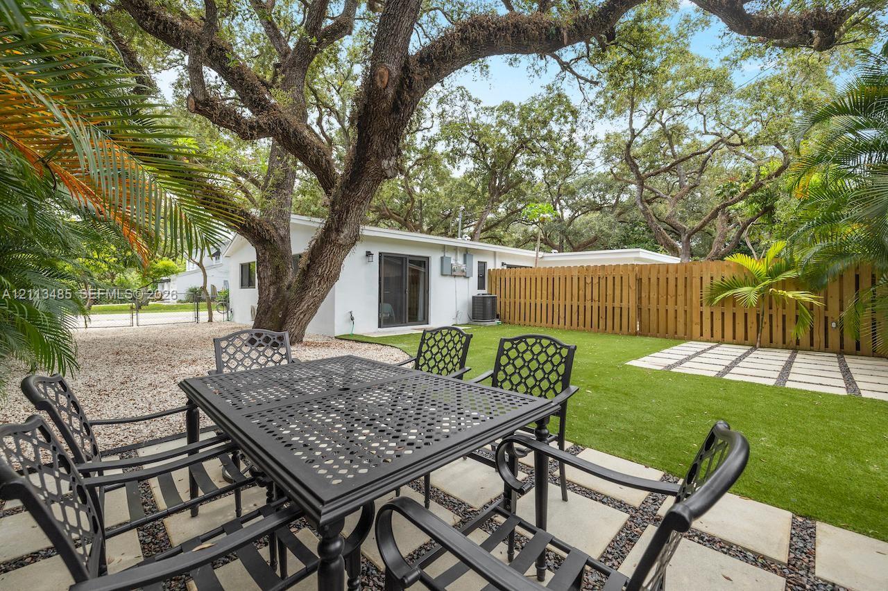 Rear yard featuring a paved patio with geometric stone pavers, low-maintenance artificial turf, a wood privacy fence, and mature trees