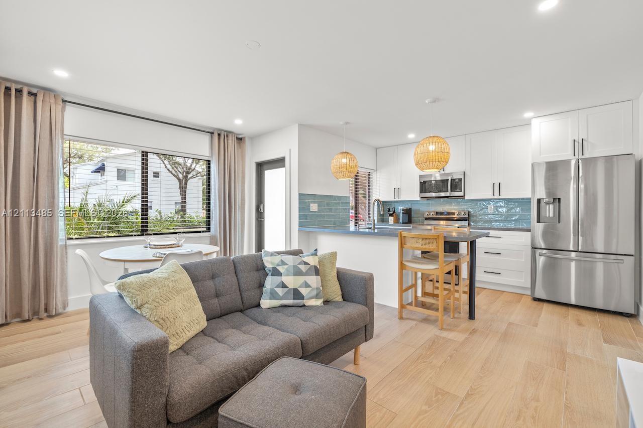 Open-concept kitchen featuring white shaker-style cabinetry, stainless steel appliances, blue tiled backsplash, and wood-finish flooring