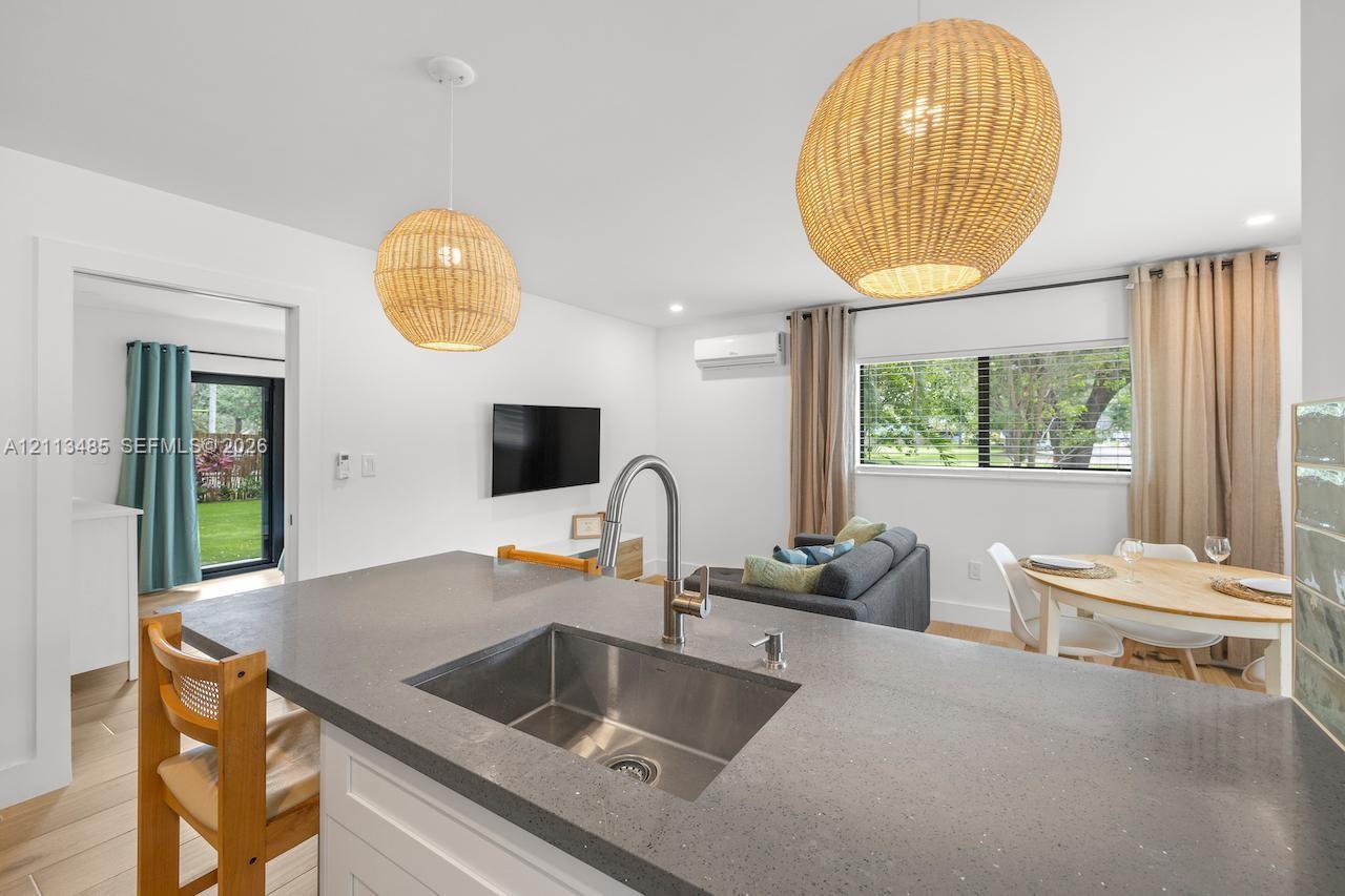 Kitchen featuring a quartz countertop, stainless steel undermount sink, high-arc faucet, dual woven pendant lighting, and wood-finish flooring