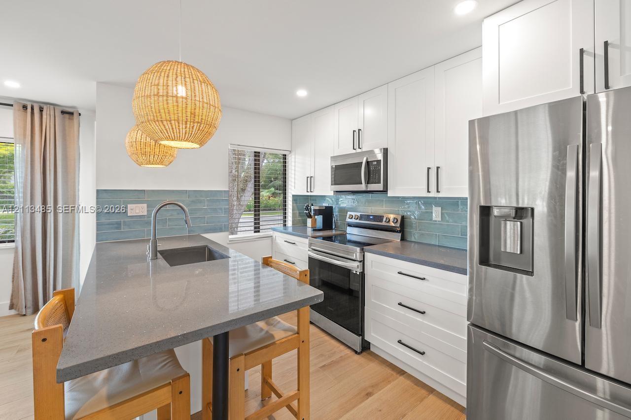 Kitchen featuring white cabinetry, grey stone-finish countertops, blue tile backsplash, stainless steel appliances, and wood-finish flooring