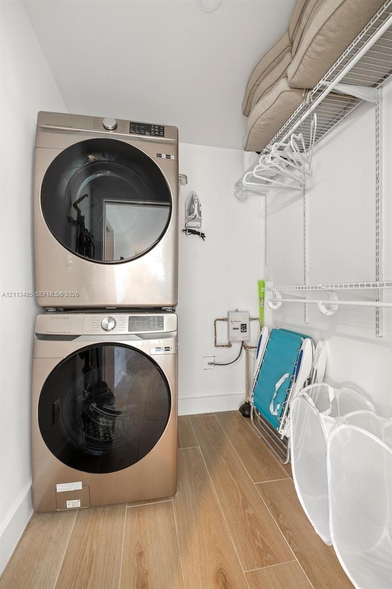 Laundry area featuring stacked appliances, wood-finish tile flooring, and integrated wire shelving