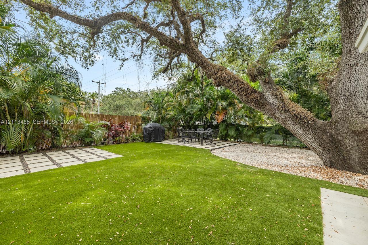 Backyard featuring synthetic turf, concrete paver accents, a gravel ground cover area, and mature canopy trees