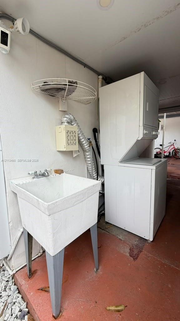 Utility area featuring a floor-mounted basin with double-handle faucet, stackable laundry unit, wall-mounted wire shelving, and recessed ceiling lighting