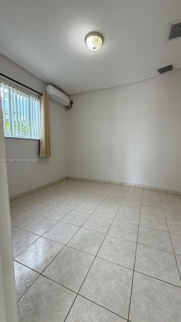 Interior space featuring neutral tile flooring, wall-mounted ductless air conditioning unit, flush-mount ceiling lighting, and vertical window blinds