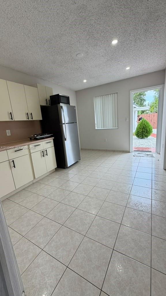 Kitchen featuring light-toned cabinetry, stainless steel refrigerator, tile flooring, recessed lighting, and direct exterior access