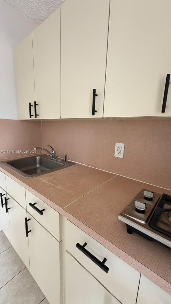 Kitchen featuring cream cabinetry, matte black hardware, solid surface countertops, a stainless steel drop-in sink, and a two-burner gas cooktop Kitchen featuring cream cabinetry, matte black hardware, solid surface countertops, a stainless steel drop-in sink, and a two-burner gas cooktop