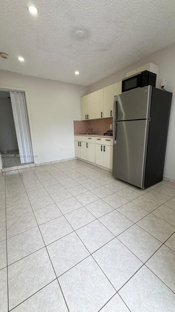 Kitchen featuring cream cabinetry, stainless steel refrigerator, built-in microwave, tile flooring, and recessed lighting Kitchen featuring cream cabinetry, stainless steel refrigerator, built-in microwave, tile flooring, and recessed lighting