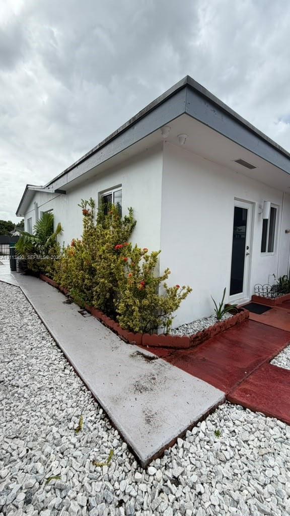 Exterior featuring a stucco facade, concrete walkway, decorative white gravel landscaping, and tiered plant beds with integrated masonry edging