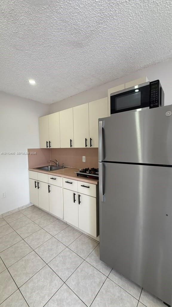 Kitchen featuring white cabinetry with matte black hardware, stainless steel refrigerator, built-in microwave, drop-in sink, and tile flooring Kitchen featuring white cabinetry with matte black hardware, stainless steel refrigerator, built-in microwave, drop-in sink, and tile flooring