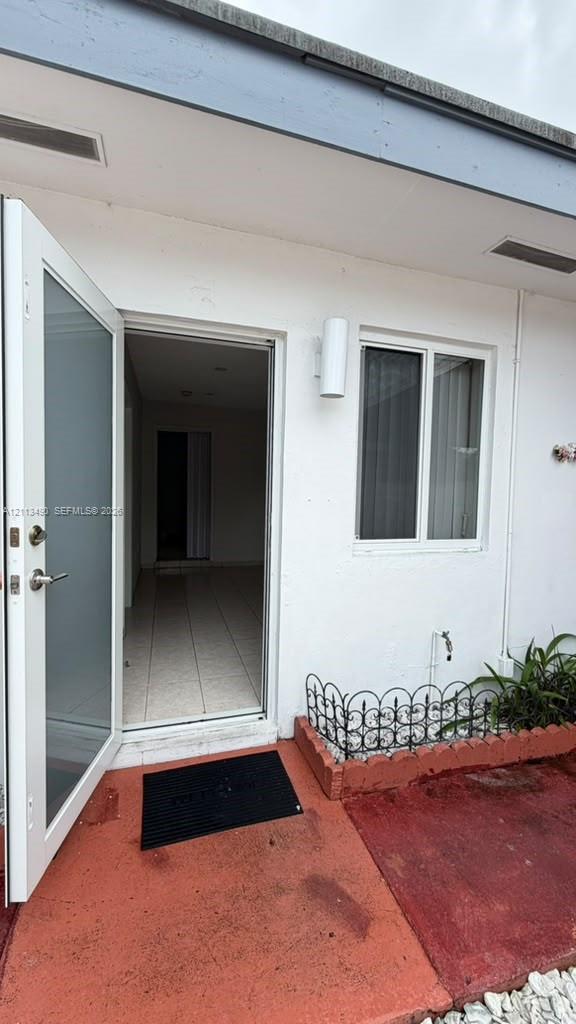 Exterior entry featuring a half-lite door, white stucco siding, dual-head cylinder wall sconce, and a decorative wrought-iron planter border Exterior entry featuring a half-lite door, white stucco siding, dual-head cylinder wall sconce, and a decorative wrought-iron planter border