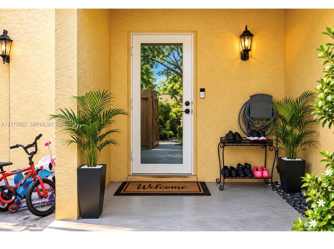 Covered entryway featuring stucco exterior walls, a full-length glass-panel door with matte black hardware, and two wall-mounted outdoor lanterns