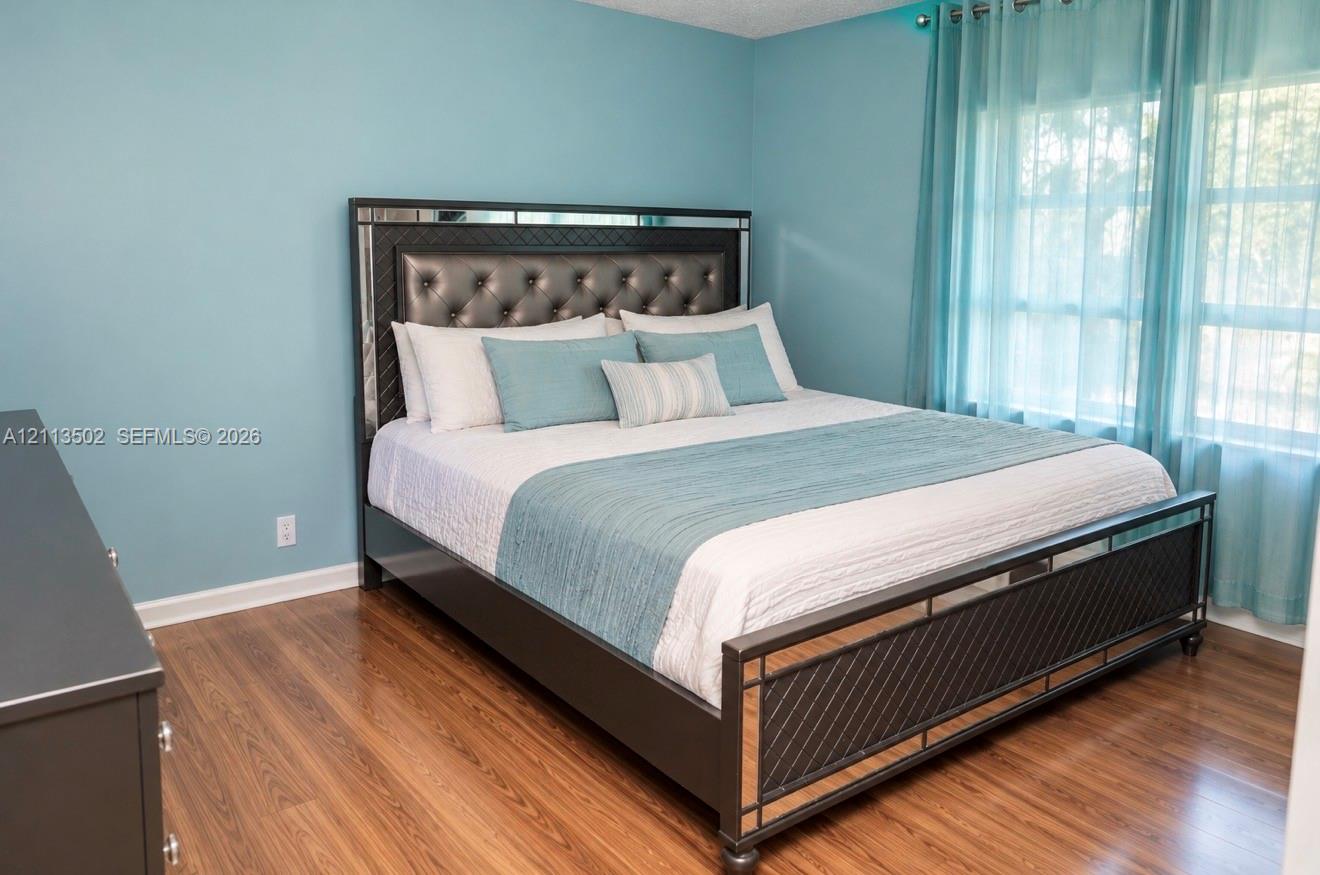 Wood-finish flooring throughout the room with multi-pane windows and sheer window treatments Wood-finish flooring throughout the room with multi-pane windows and sheer window treatments