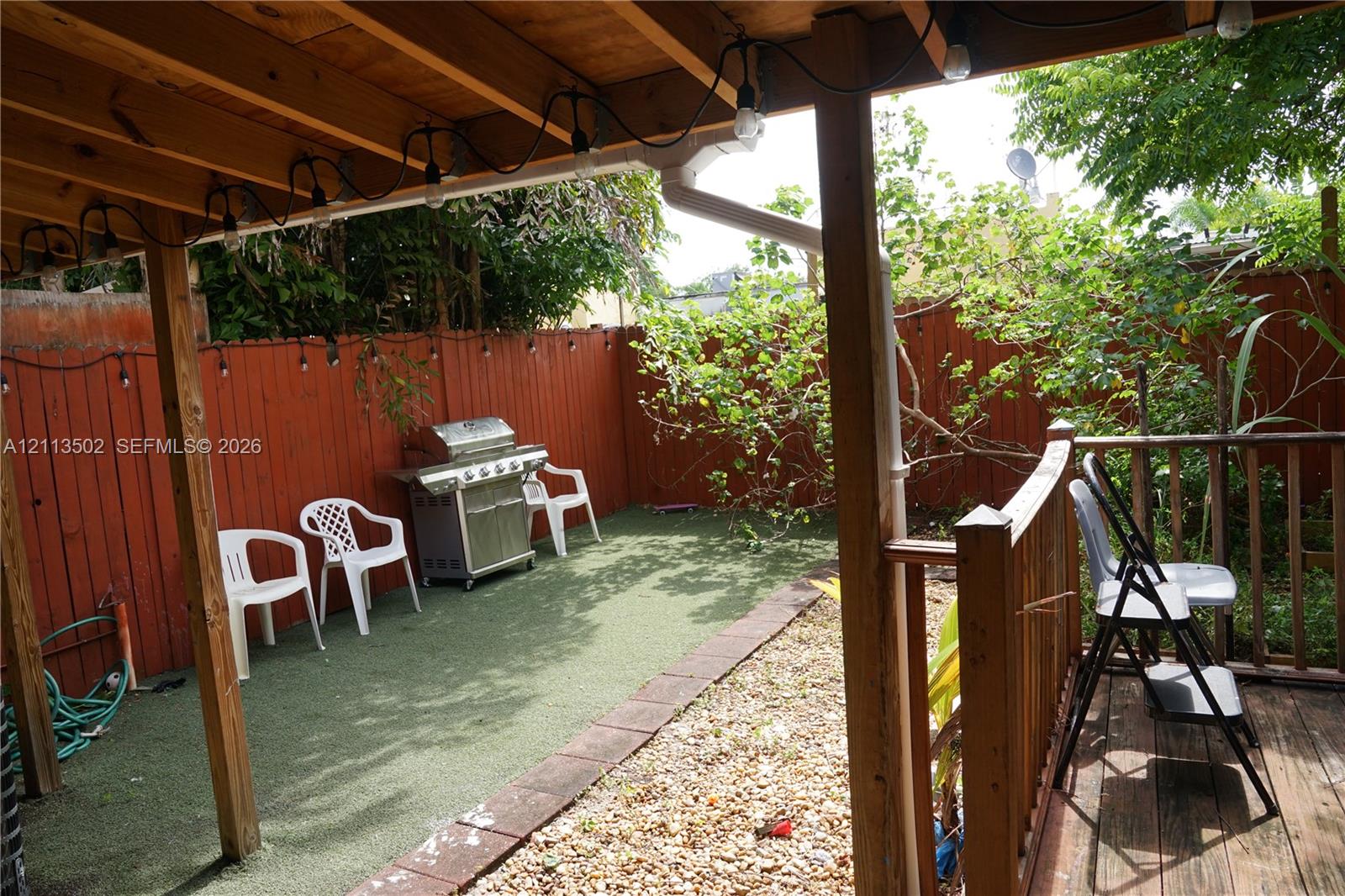 Covered patio with wood framing, synthetic turf ground cover, perimeter wood fencing, and natural gravel ground cover Covered patio with wood framing, synthetic turf ground cover, perimeter wood fencing, and natural gravel ground cover