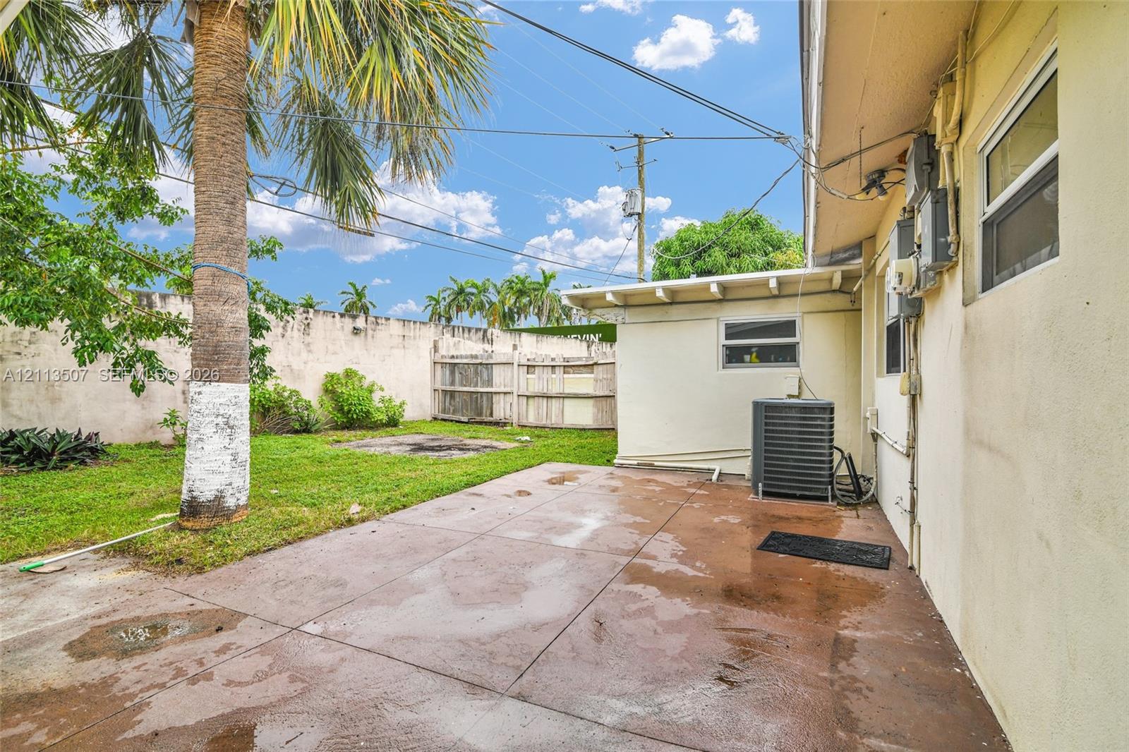 Rear exterior space featuring a concrete patio, perimeter masonry wall, wood privacy fencing, and mature palm tree