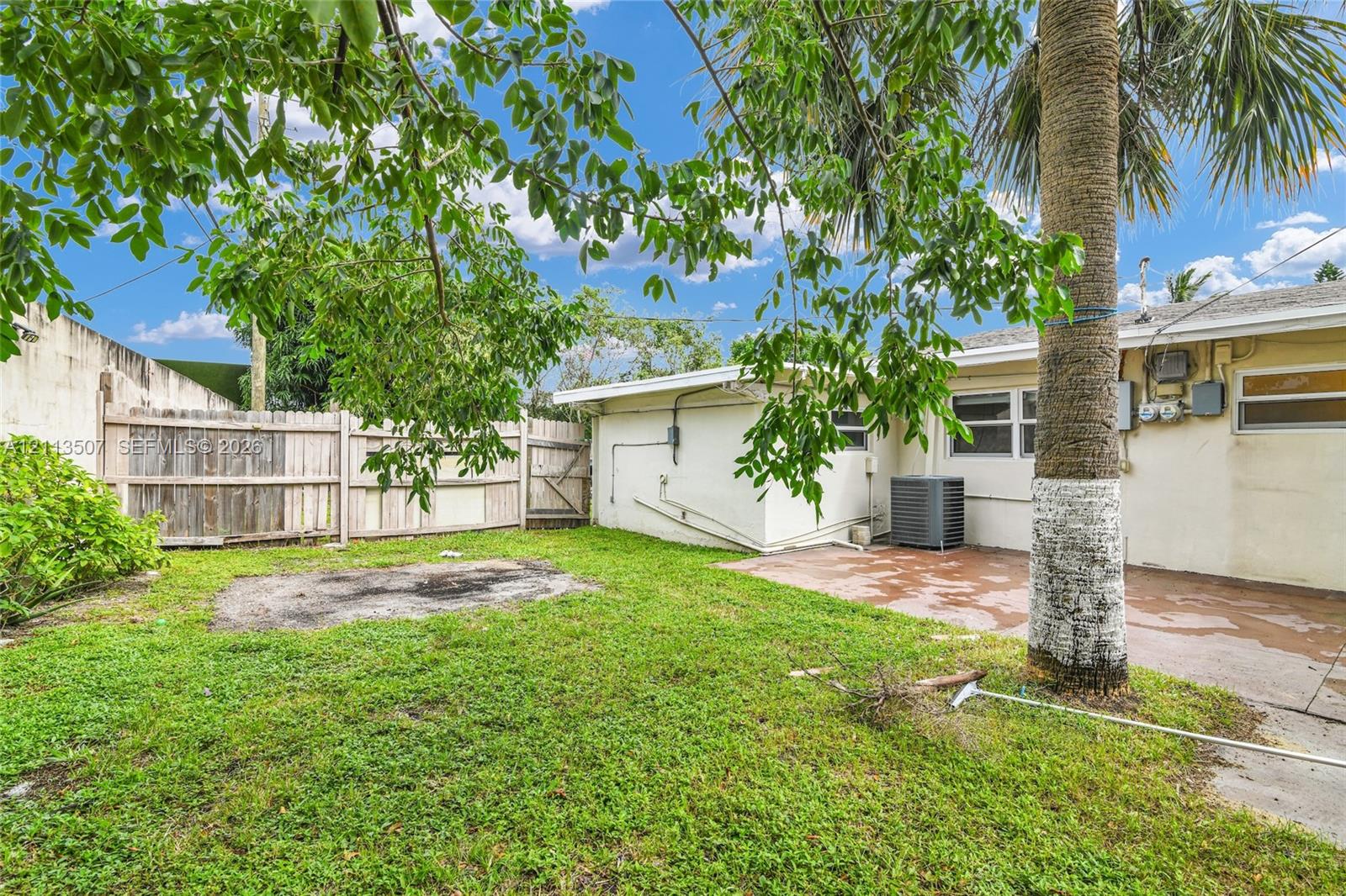Backyard featuring a concrete patio, wood privacy fencing, grass lawn, and mature palm tree