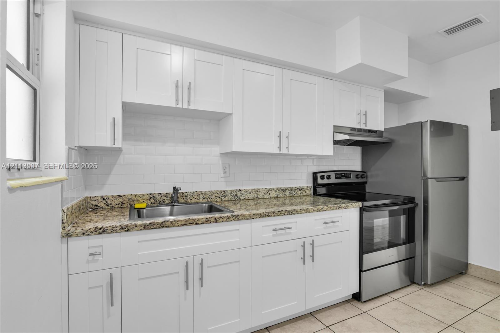 Kitchen featuring white shaker-style cabinetry, stone-finish countertops, subway tile backsplash, stainless steel appliances, and tile flooring