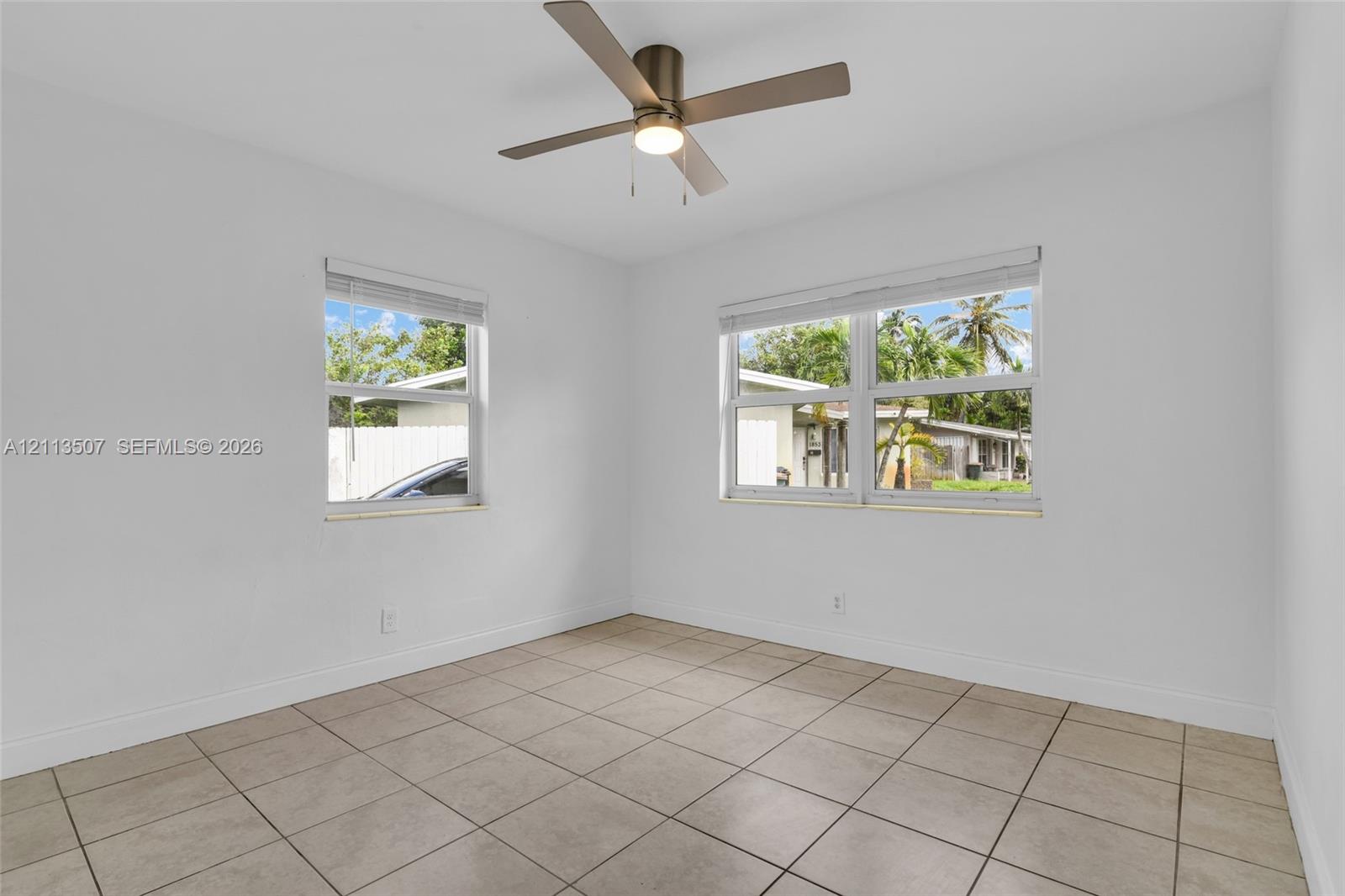 Neutral-toned ceramic tile flooring, metallic ceiling fan with integrated lighting, and dual windows with horizontal blinds