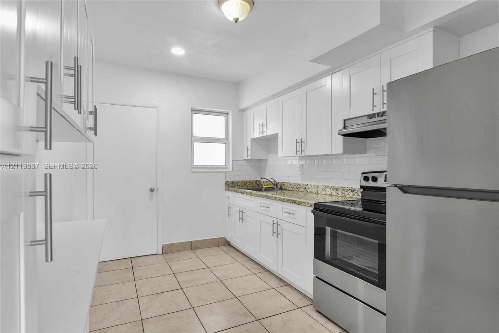 Kitchen featuring white shaker-style cabinetry, stone-finish countertops, subway tile backsplash, stainless steel appliances, and ceramic tile flooring