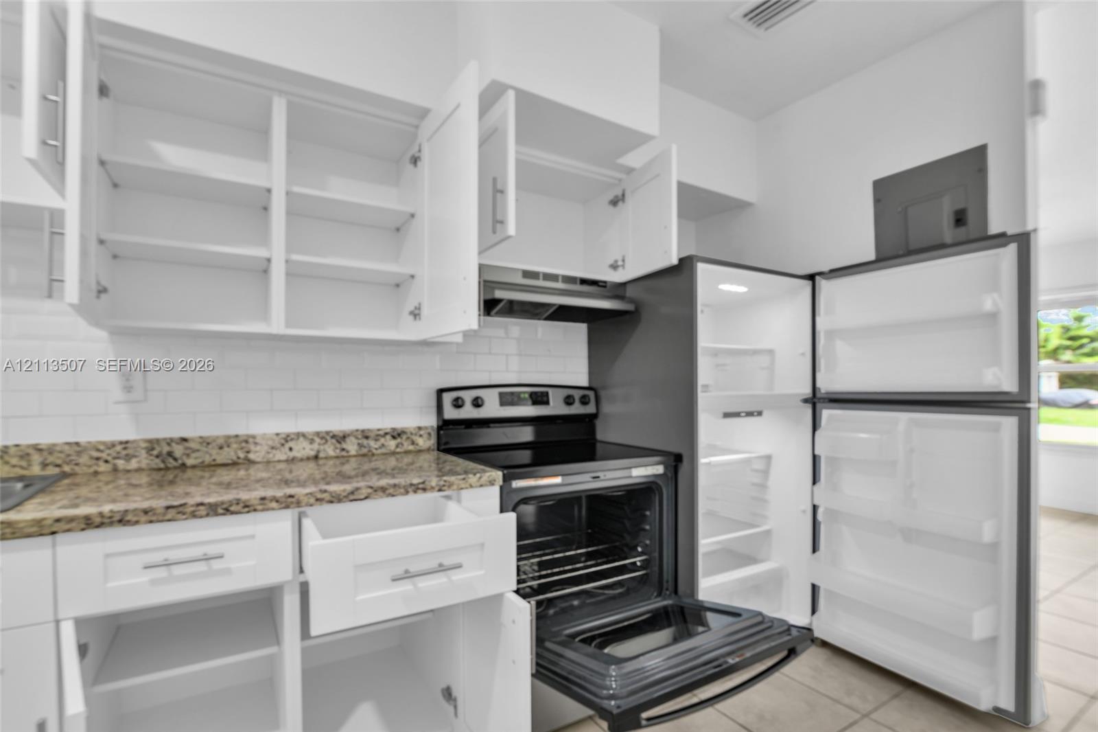 Kitchen featuring white cabinetry, stone-finish countertops, subway tile backsplash, and stainless steel appliances including a range and refrigerator