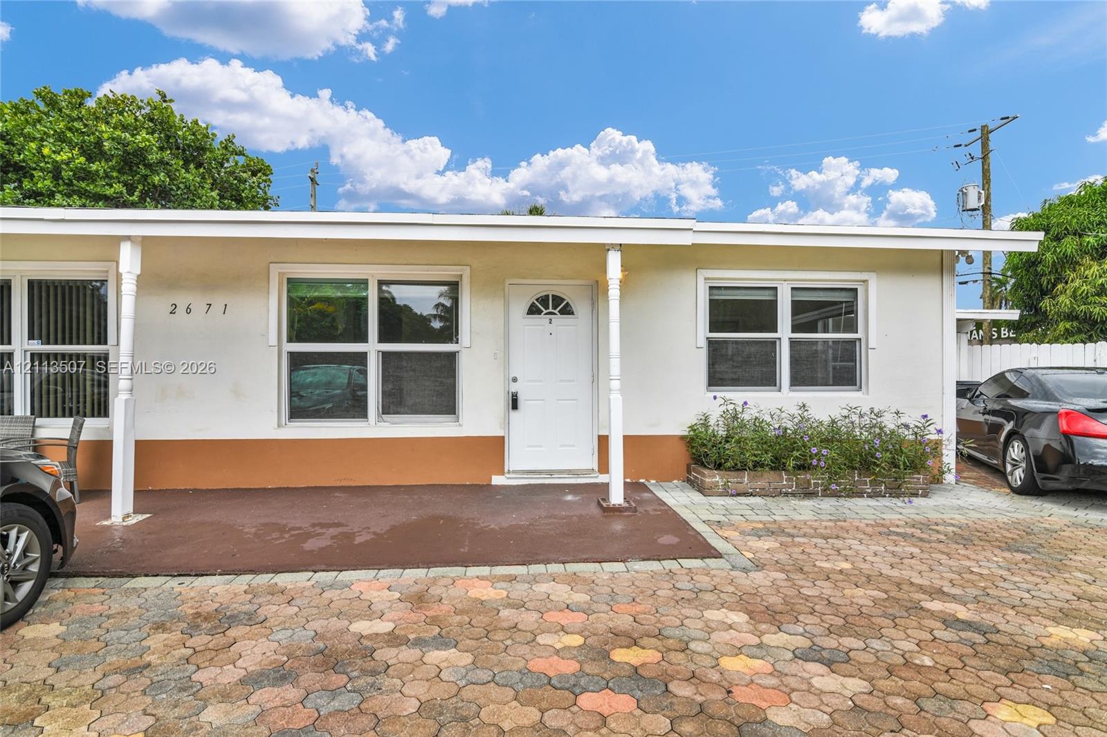 Single-story exterior featuring a covered front porch, multi-pane windows, a paver driveway, and an integrated stone-faced garden bed