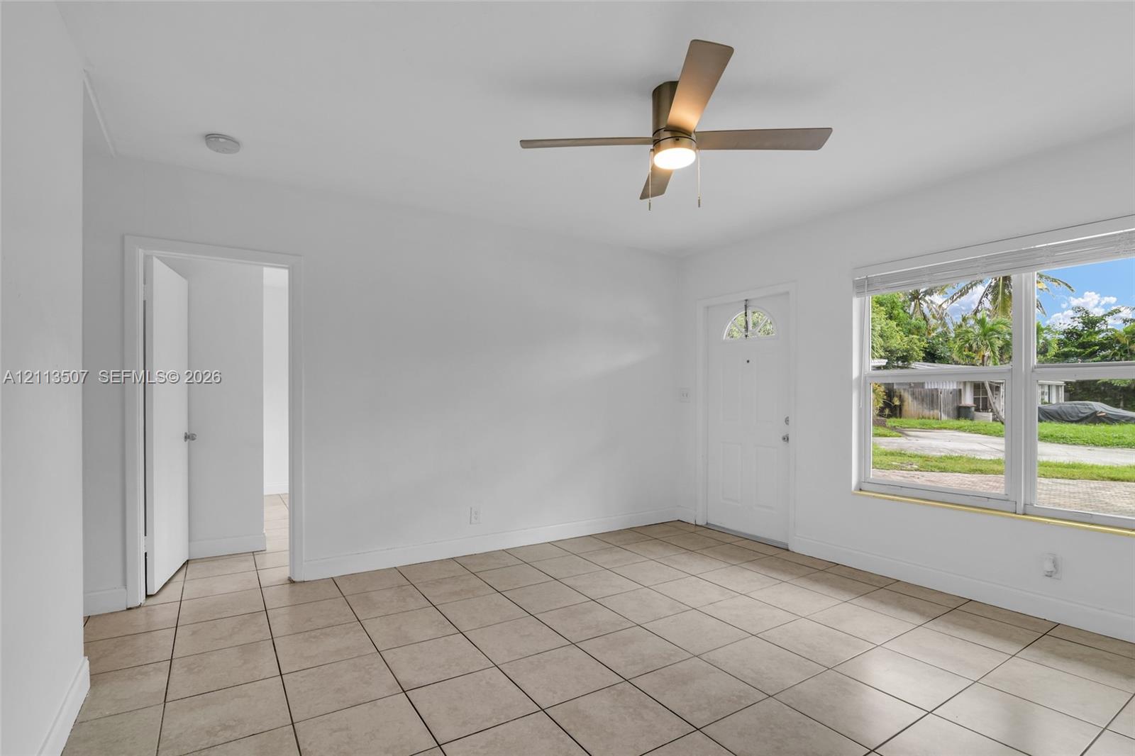 Neutral-toned tile flooring, minimalist white walls, ceiling-mounted fan with integrated lighting, and white exterior door with glass insert Neutral-toned tile flooring, minimalist white walls, ceiling-mounted fan with integrated lighting, and white exterior door with glass insert