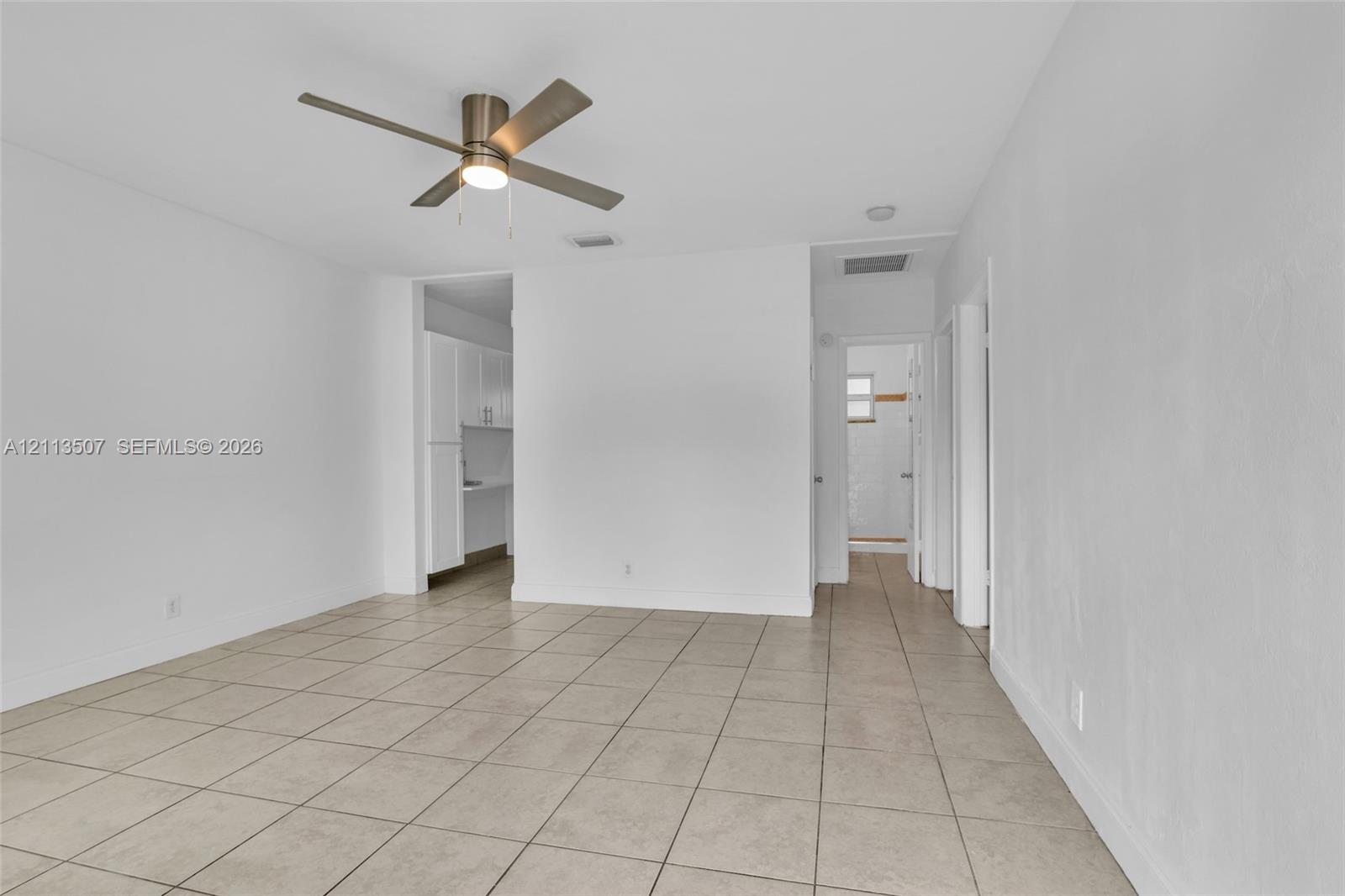 Neutral interior featuring tile flooring, smooth wall finishes, and a ceiling-mounted light fixture with a fan Neutral interior featuring tile flooring, smooth wall finishes, and a ceiling-mounted light fixture with a fan