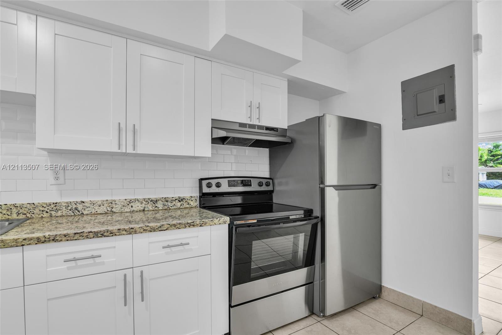 Kitchen featuring white Shaker-style cabinetry, stone countertops, a white subway tile backsplash, and stainless steel appliances