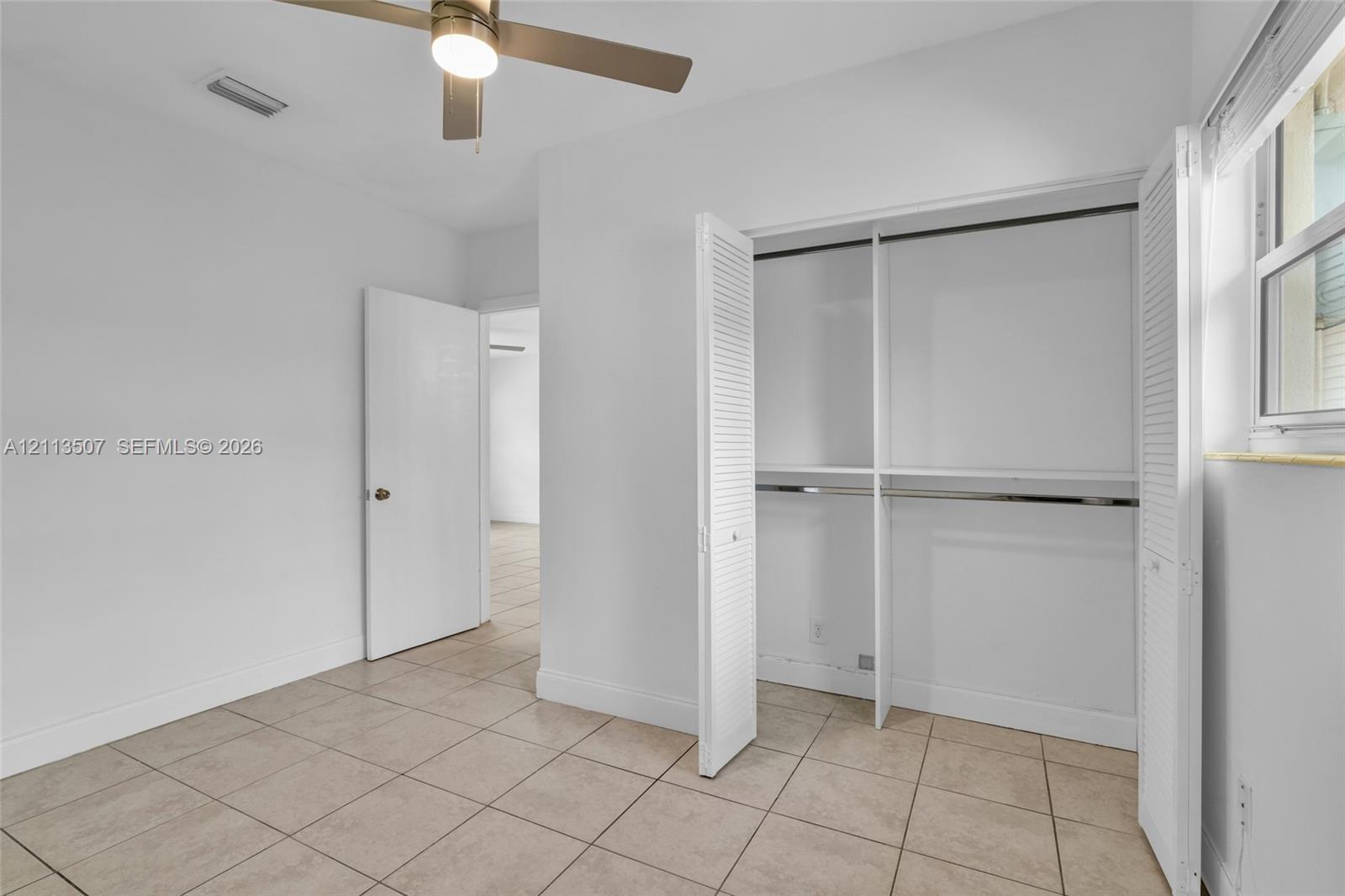 Neutral-toned ceramic tile flooring, closet with bi-fold louvered doors, ceiling fan with integrated lighting, and window with horizontal blinds Neutral-toned ceramic tile flooring, closet with bi-fold louvered doors, ceiling fan with integrated lighting, and window with horizontal blinds