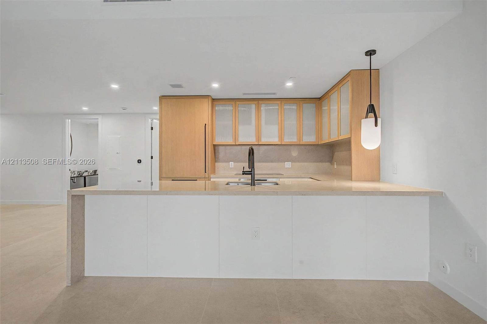 Kitchen featuring wood cabinetry with glass-panel upper doors, a stone-finish waterfall edge island, a matte black high-arch faucet, integrated appliances, and recessed ceiling lighting