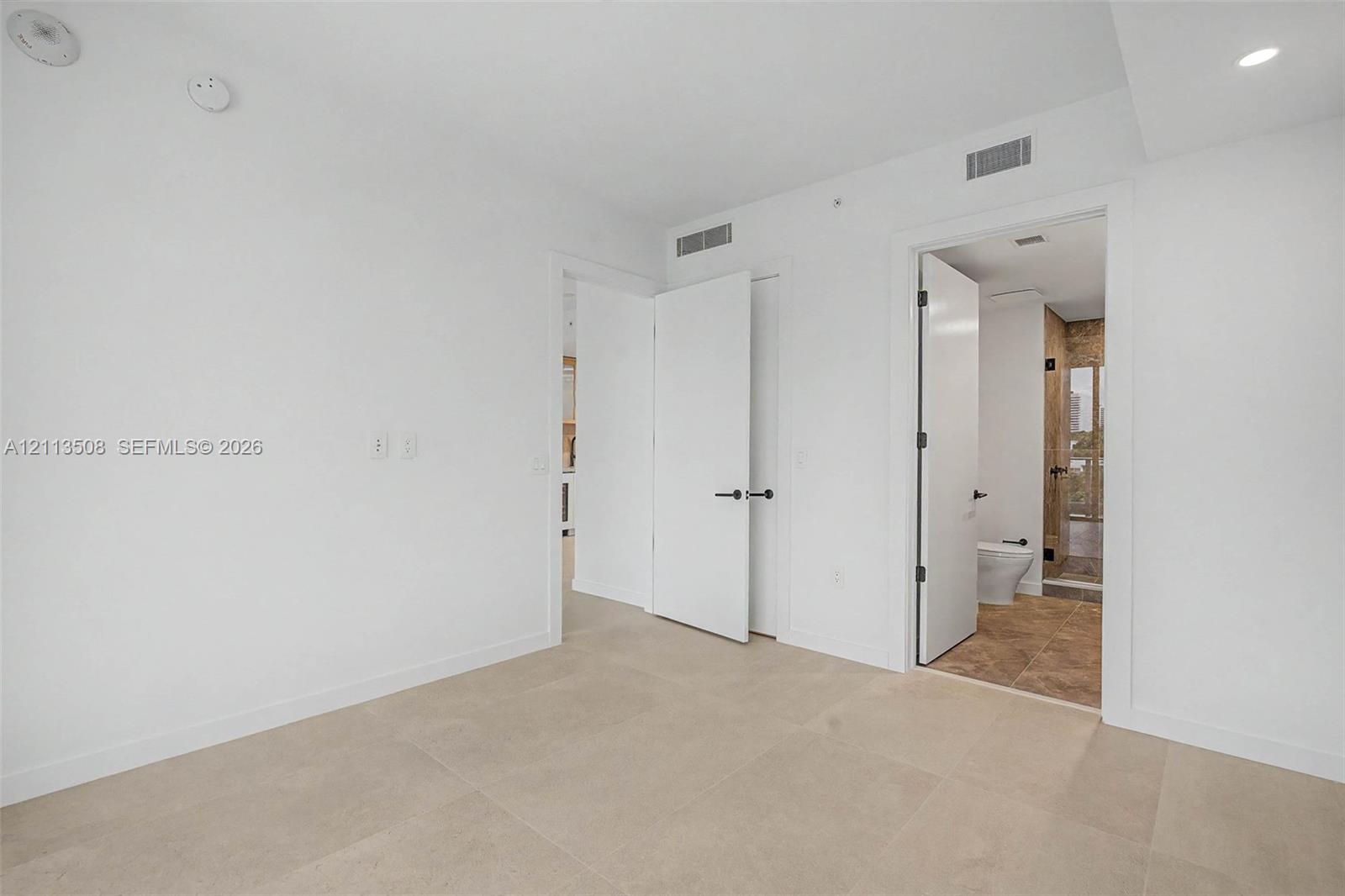Large-format neutral floor tiling, recessed lighting, and solid-core interior doors with matte black hardware