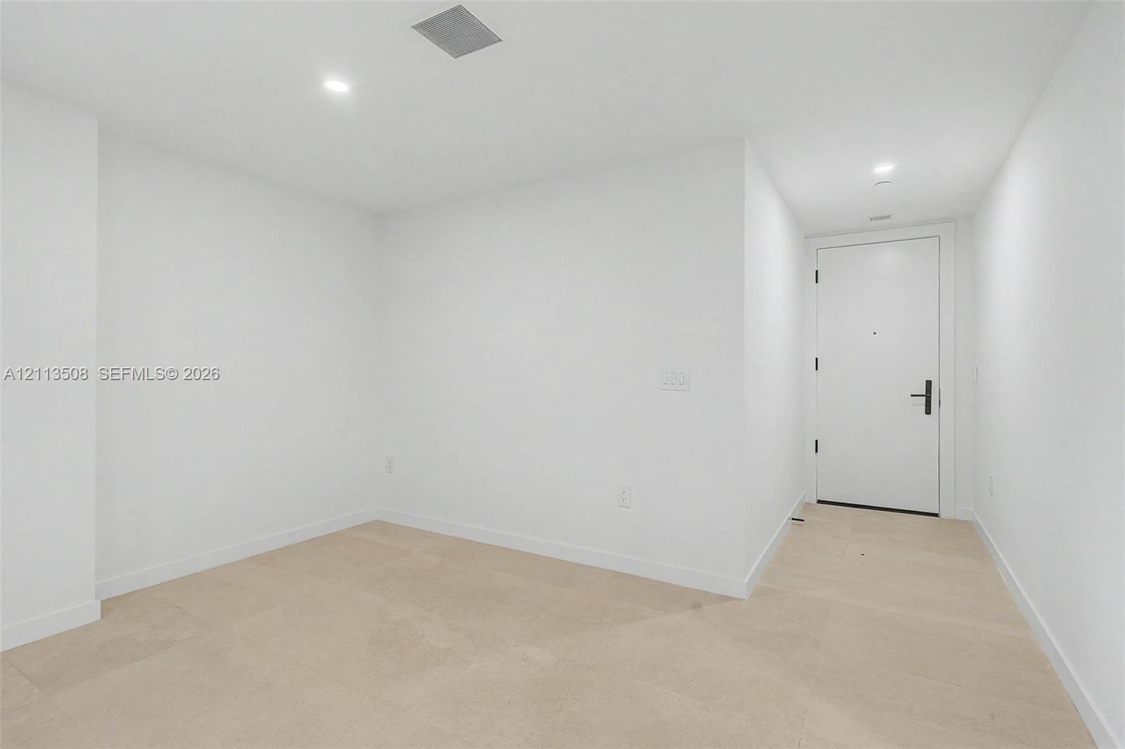 Neutral interior featuring light-toned flooring, recessed lighting, and a solid-core door with matte black hardware