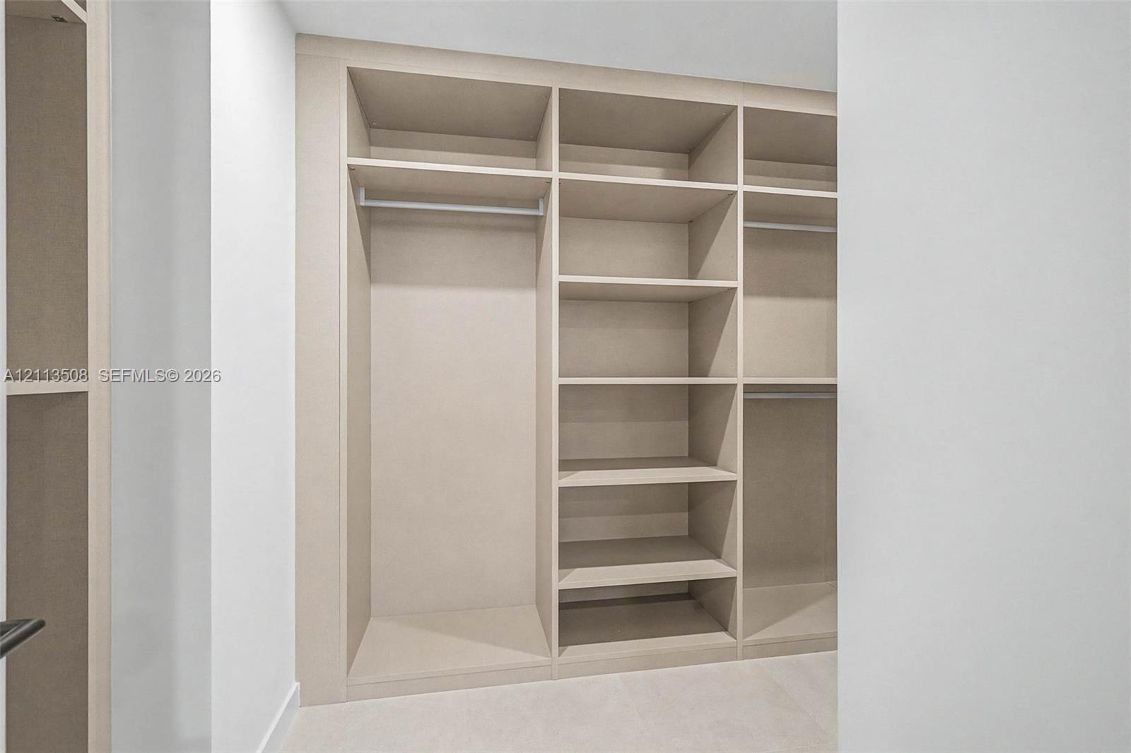Custom built-in storage featuring integrated shelving, vertical partitions, and horizontal hanging rods with a neutral finish