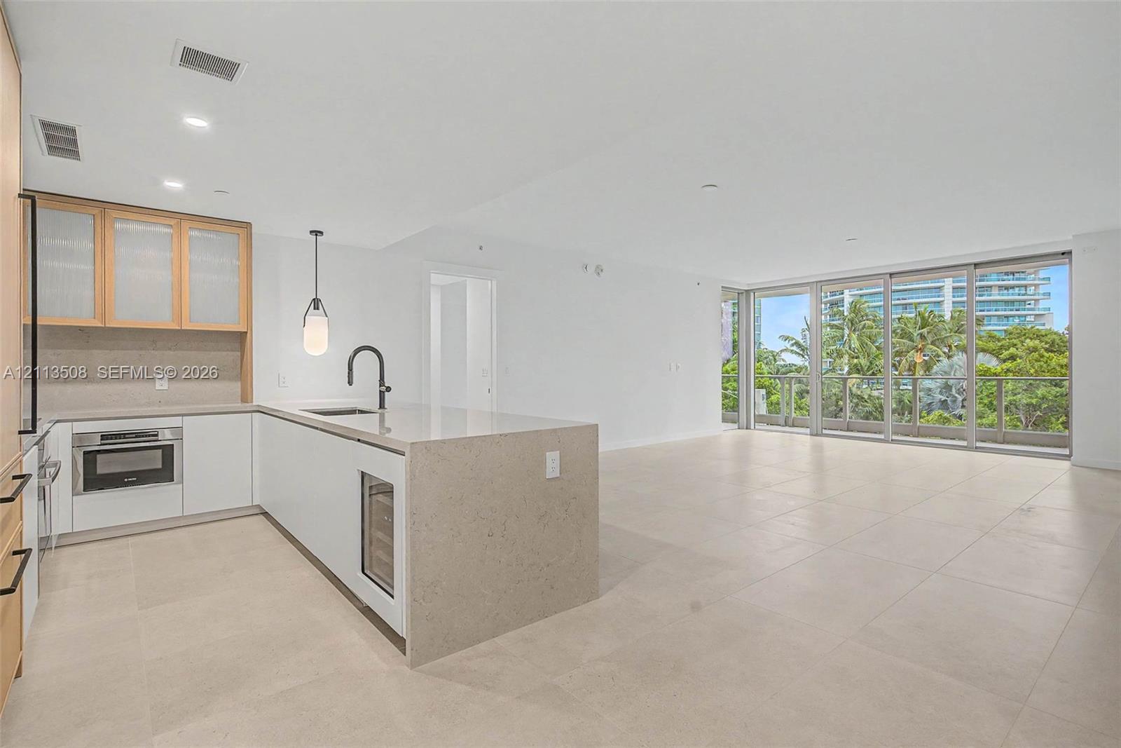 Kitchen featuring stone countertops, a waterfall-edge island, built-in beverage refrigerator, matte black faucet, and large-format tile flooring