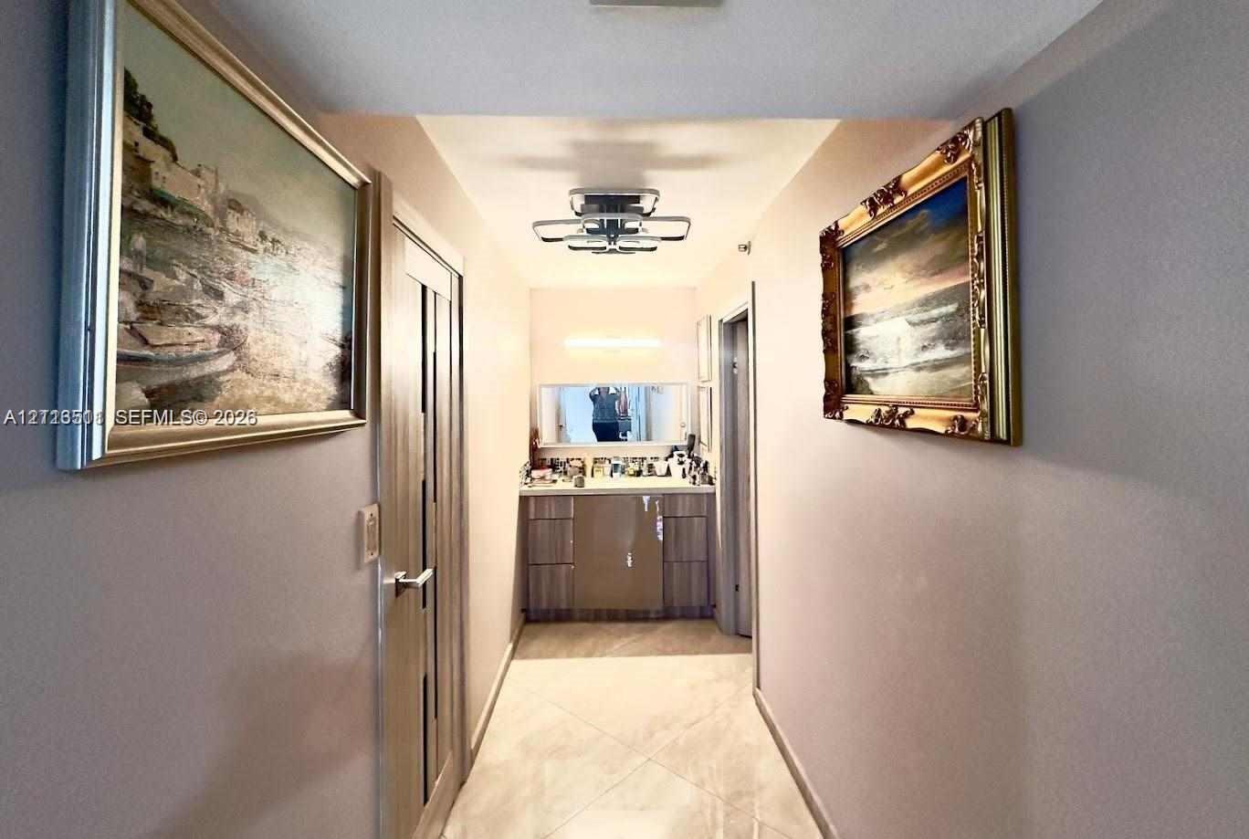 Hallway featuring neutral-toned walls, tile flooring, a geometric flush-mount light fixture, and a built-in vanity with a stone countertop and rectangular mirror