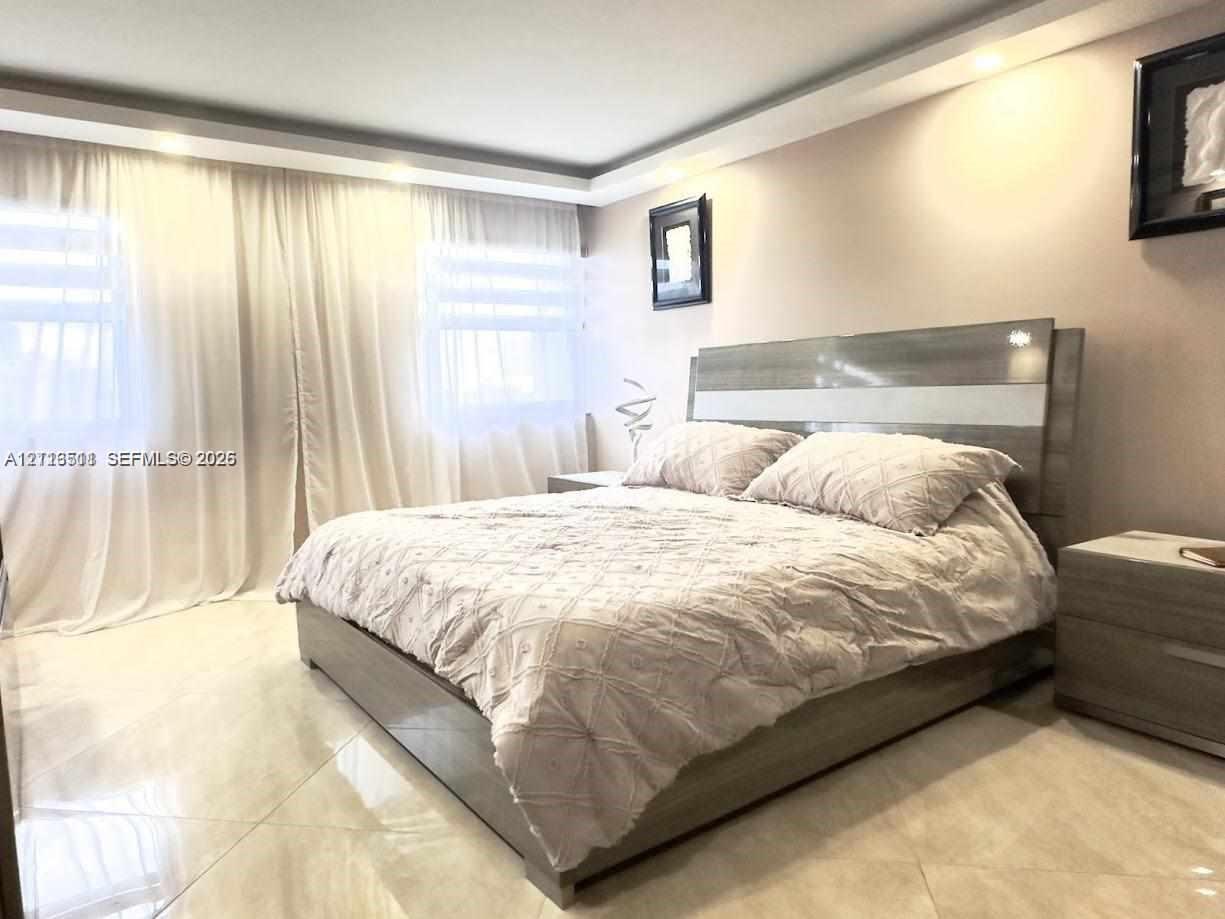 Large-format tile flooring, tray ceiling with recessed lighting, and wall-to-wall drapery