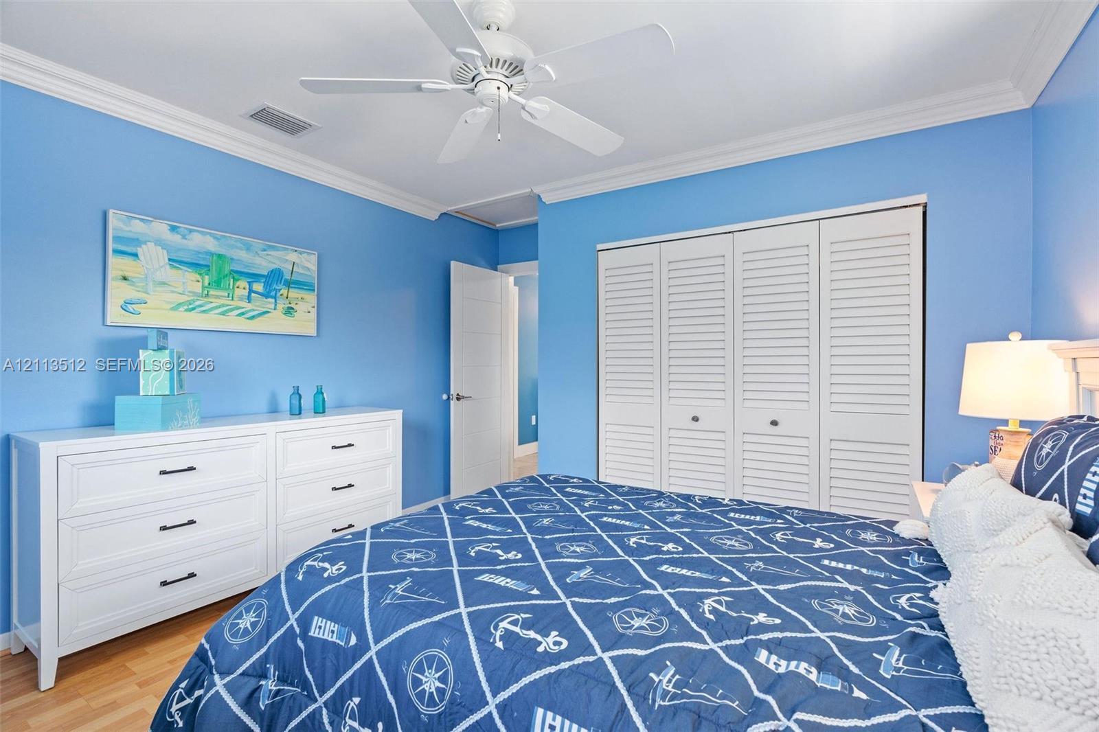 Room featuring wood-finish flooring, white louvered-door closets, crown molding, and a white ceiling fan