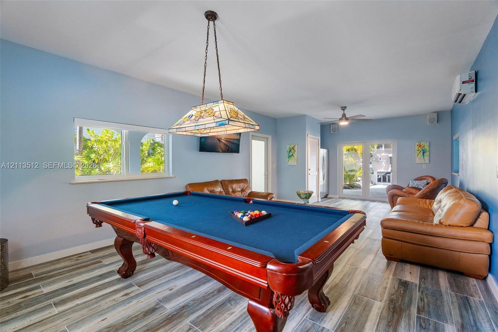 Spacious room featuring wood-finish flooring, stained-glass hanging pendant light, dual-pane windows, and glass-paneled double doors