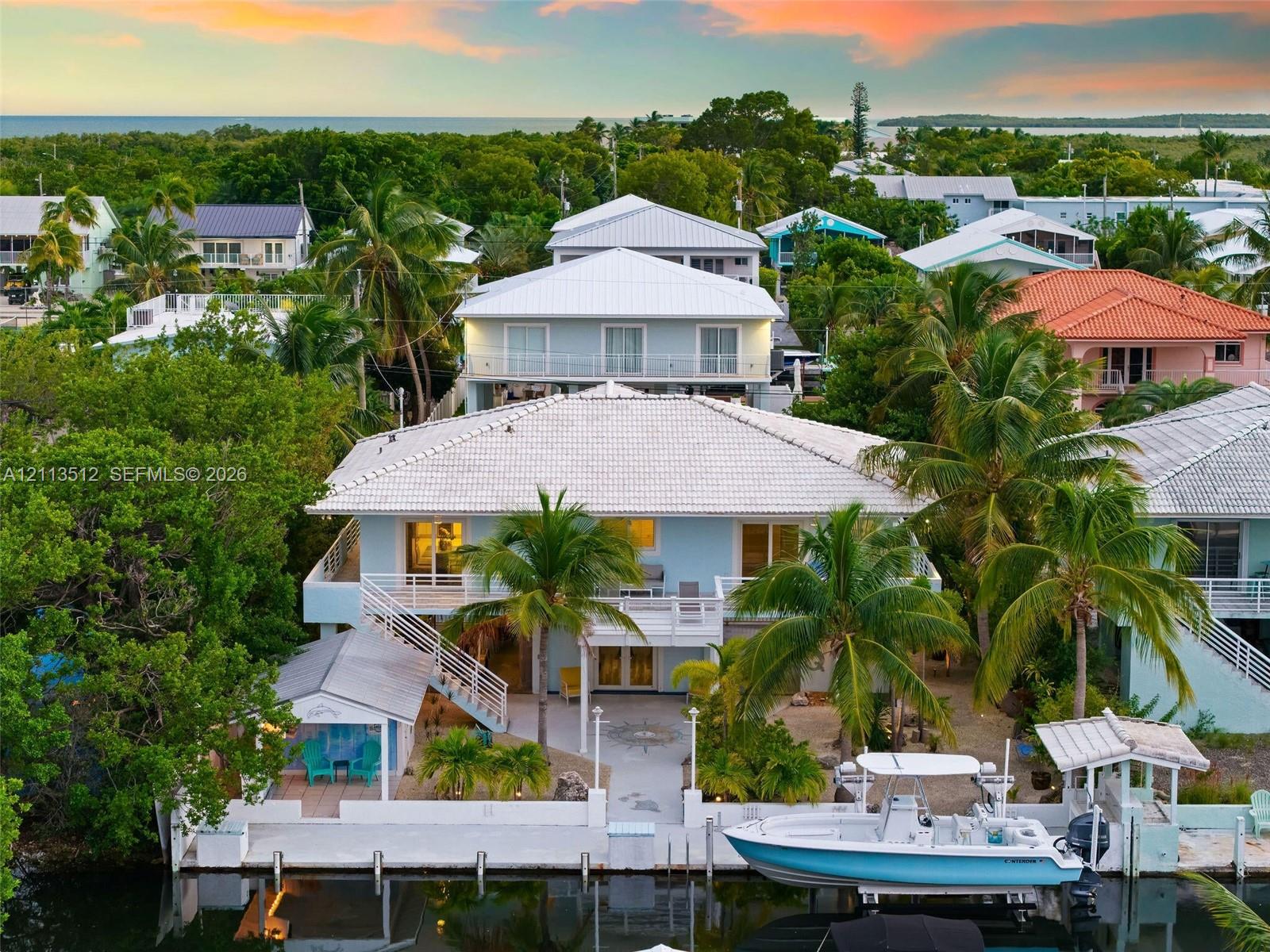 Waterfront property featuring a private concrete dock, multilevel balconies, tile roofing, and mature palm landscaping