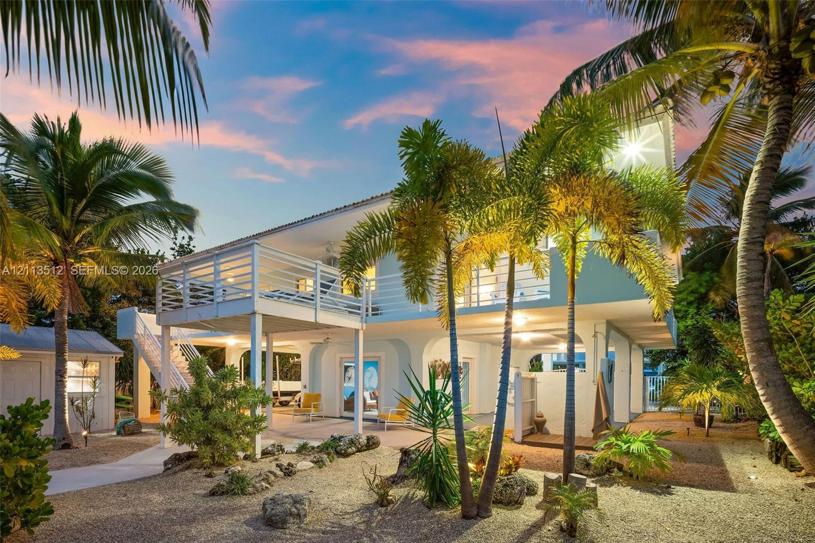 Elevated residence featuring a wrap-around balcony, arched ground-level architecture, external staircase, and tropical landscaping