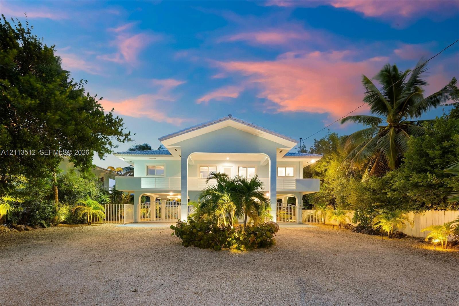 Elevated residence featuring a covered front porch, support columns, white metal railings, and a gravel driveway