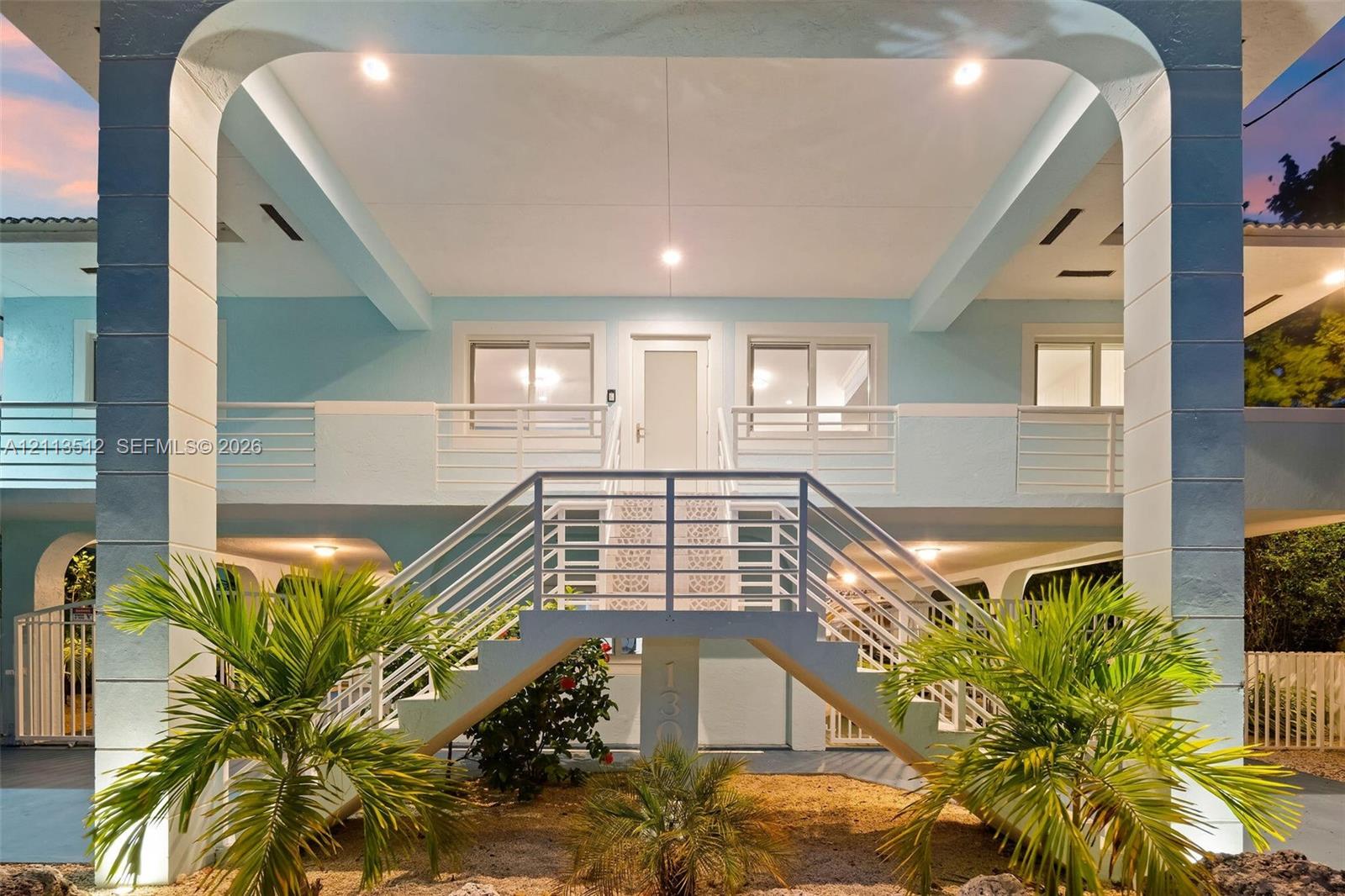 Elevated structure featuring a staircase with metal railings, arched support columns, recessed ceiling lighting, and second-level balcony