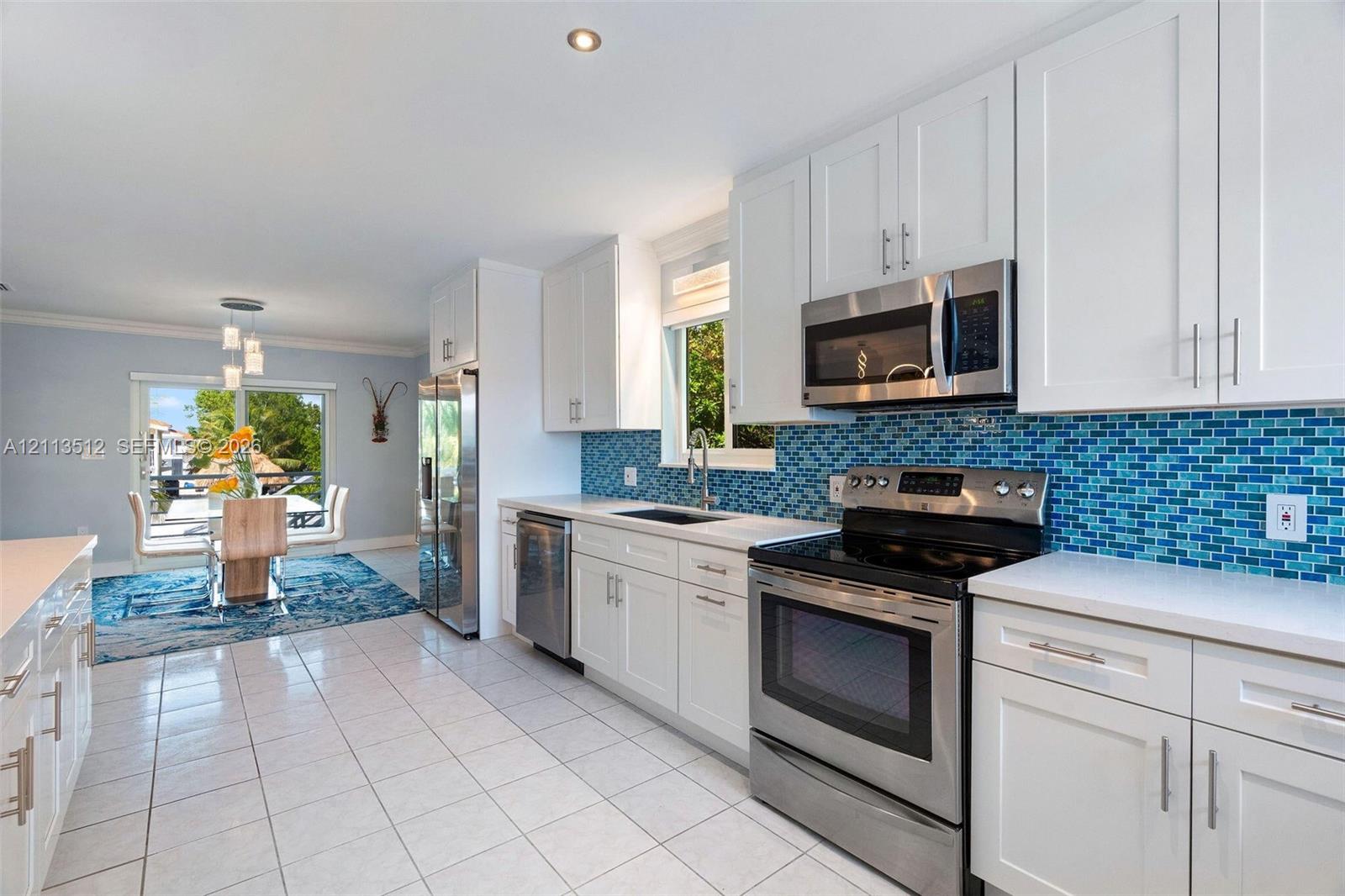 Kitchen featuring white shaker-style cabinetry, stainless steel appliances, blue glass tile backsplash, white countertops, and tile flooring