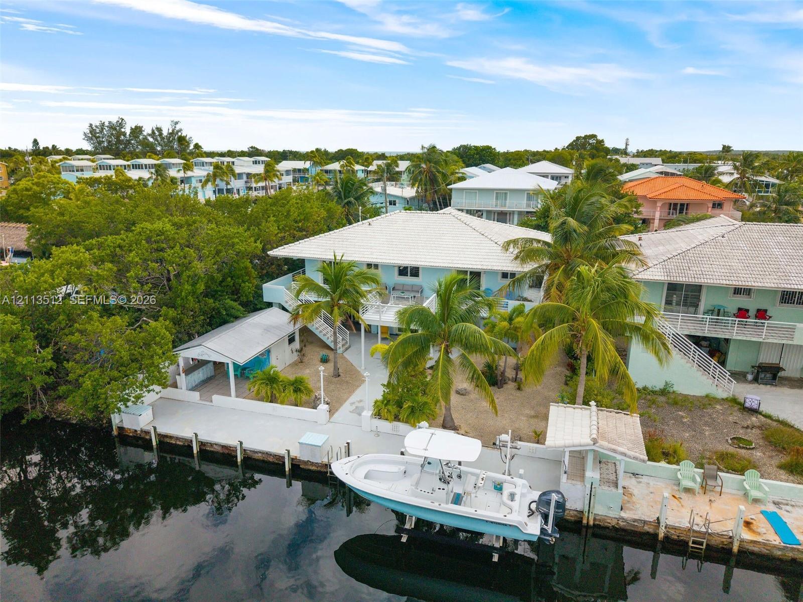 Waterfront property featuring a private boat dock, concrete bulkhead, covered outdoor living structure, and mature palm trees