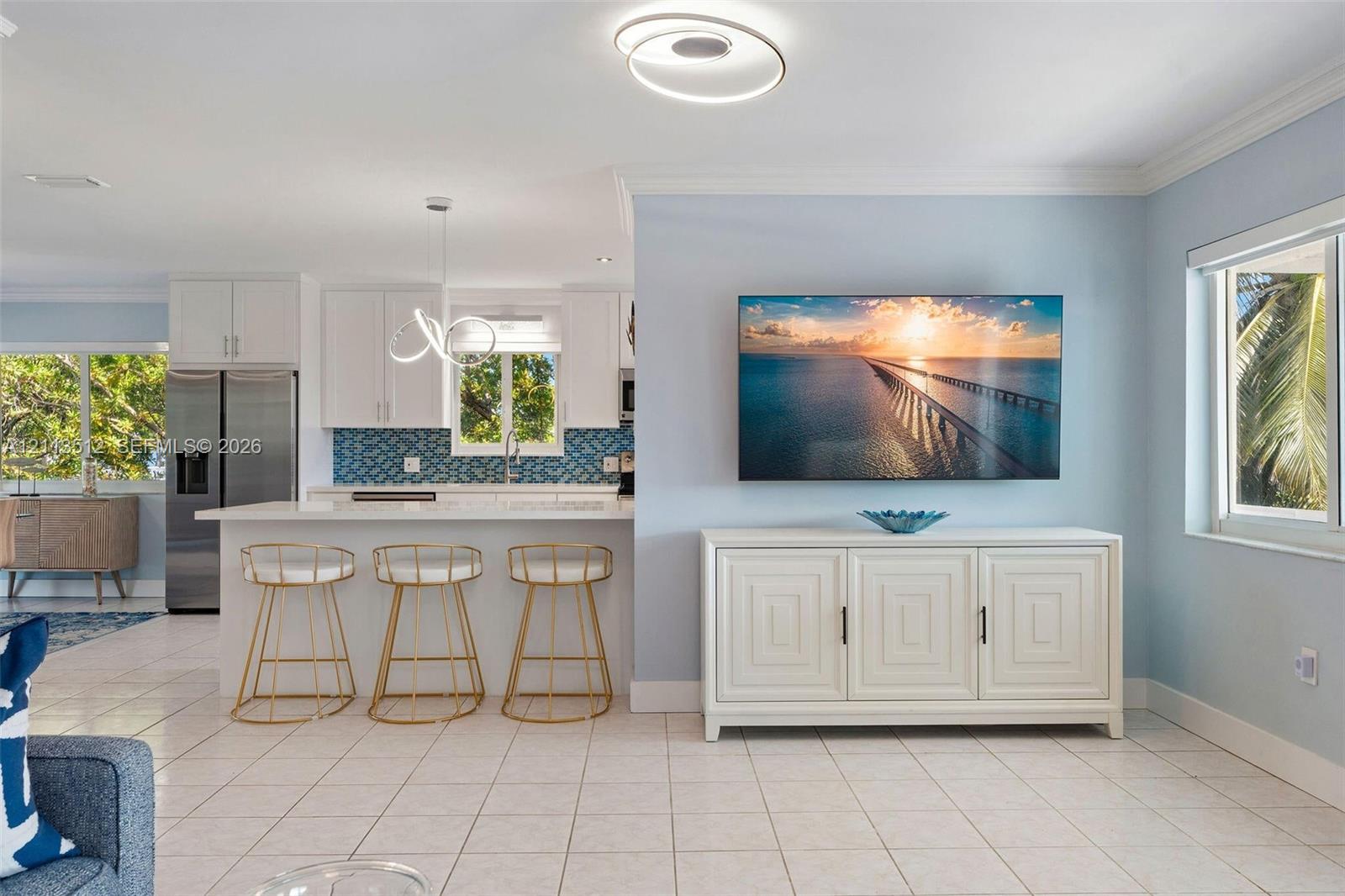 Open-concept interior featuring a kitchen with white cabinetry, a breakfast bar with geometric tile backsplash, stainless steel appliances, circular LED lighting fixtures, and tile flooring