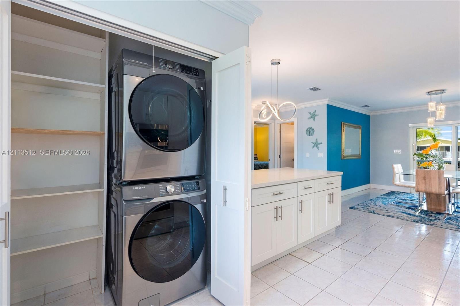 Laundry area featuring a stacked stainless steel washer and dryer, built-in shelving, white cabinetry with stone countertops, and tile flooring