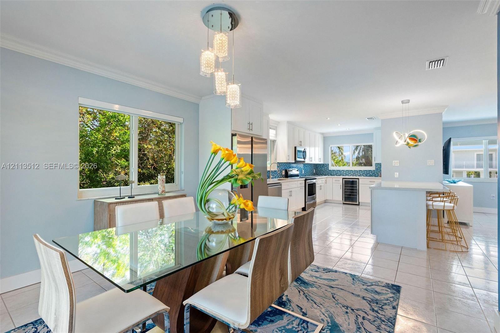 Open-concept kitchen and dining area featuring white shaker-style cabinetry, a central island with bar seating, tile flooring, and multi-light geometric pendant fixtures