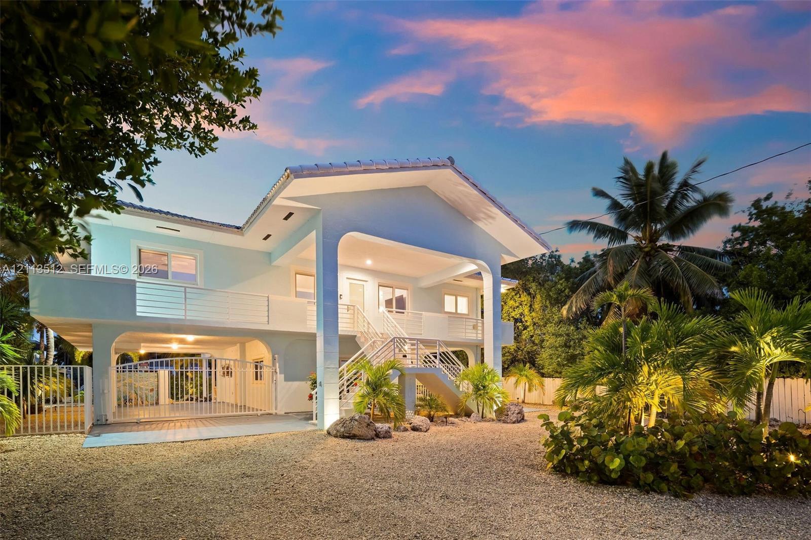 Elevated residence featuring a covered entryway, second-story balcony with metal railings, arched architectural detailing, and a ground-level gated carport