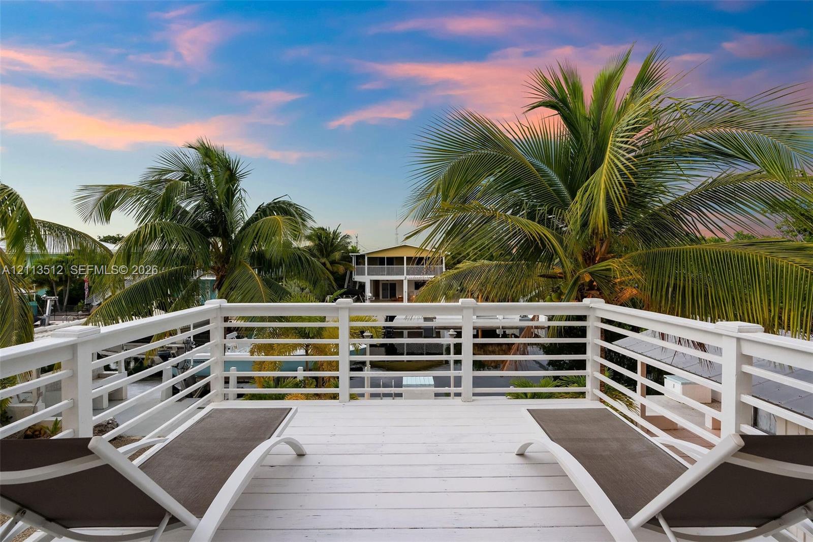 Elevated deck with white horizontal railing and wood-plank flooring, accented by mature palm trees