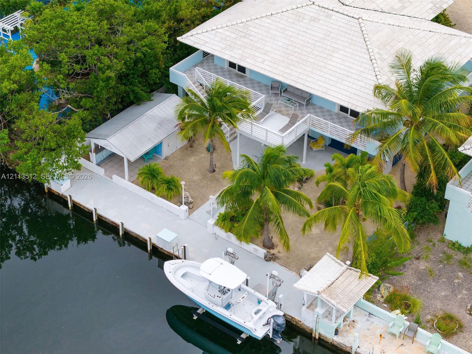 Waterfront property featuring a private concrete dock with boat lift, covered outdoor pavilion, elevated wrap-around balcony, and tile roof