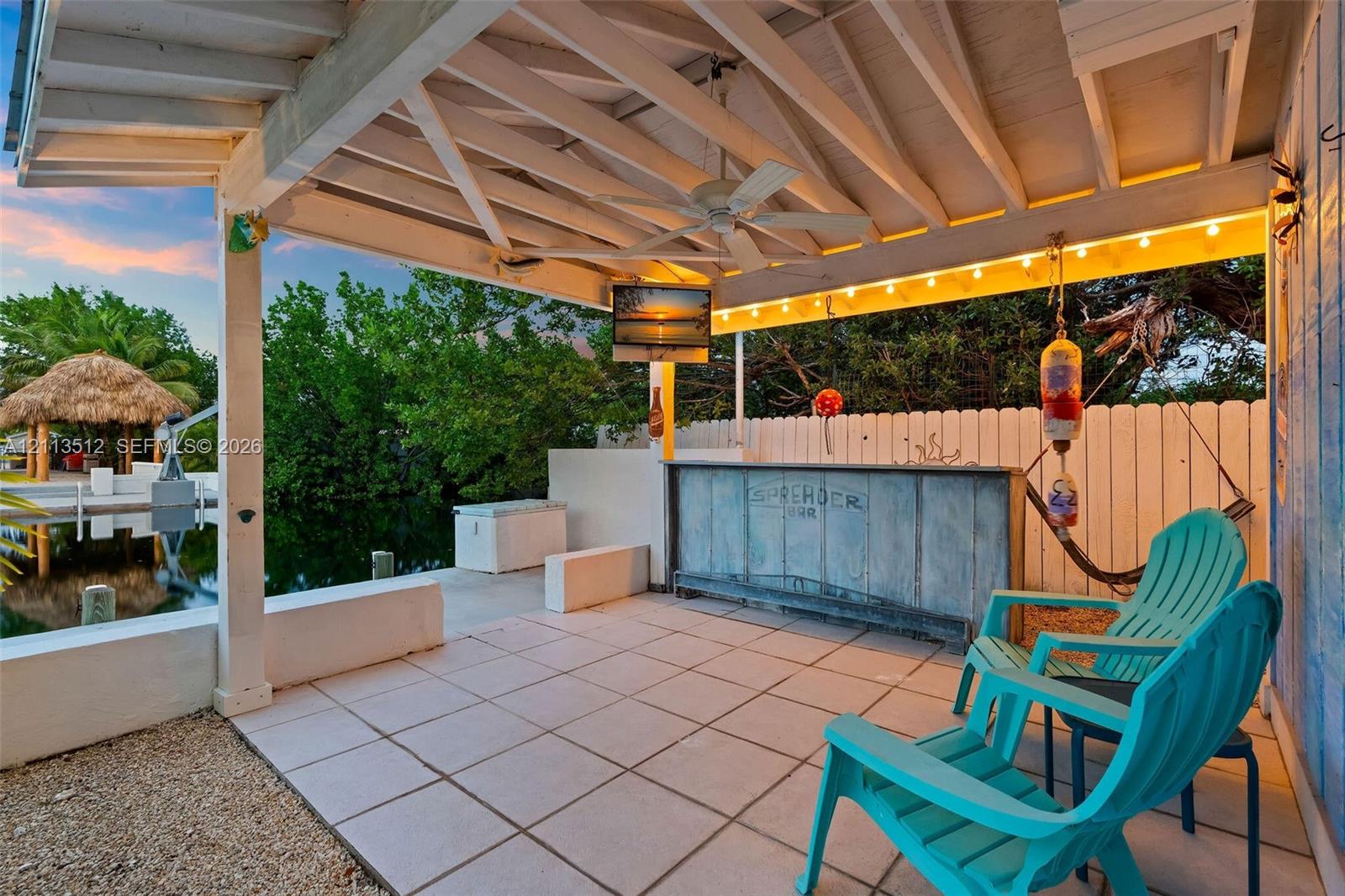 Covered waterfront patio featuring a built-in bar, tile flooring, exposed beamed ceiling with a mounted ceiling fan, and direct access to a concrete seawall